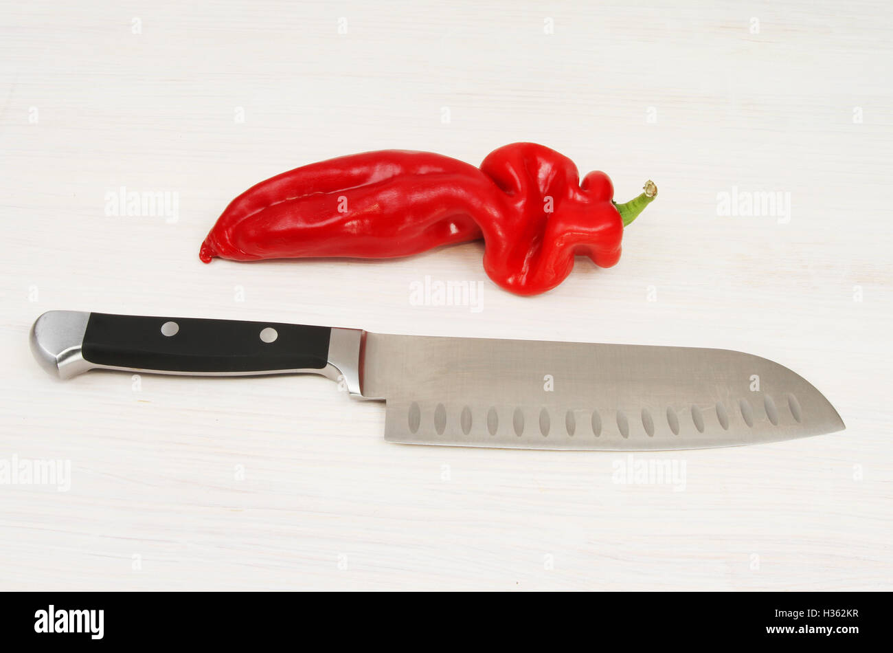 Spitzen, rote Paprika und ein Messer auf weiß lackiertem Holz Stockfoto