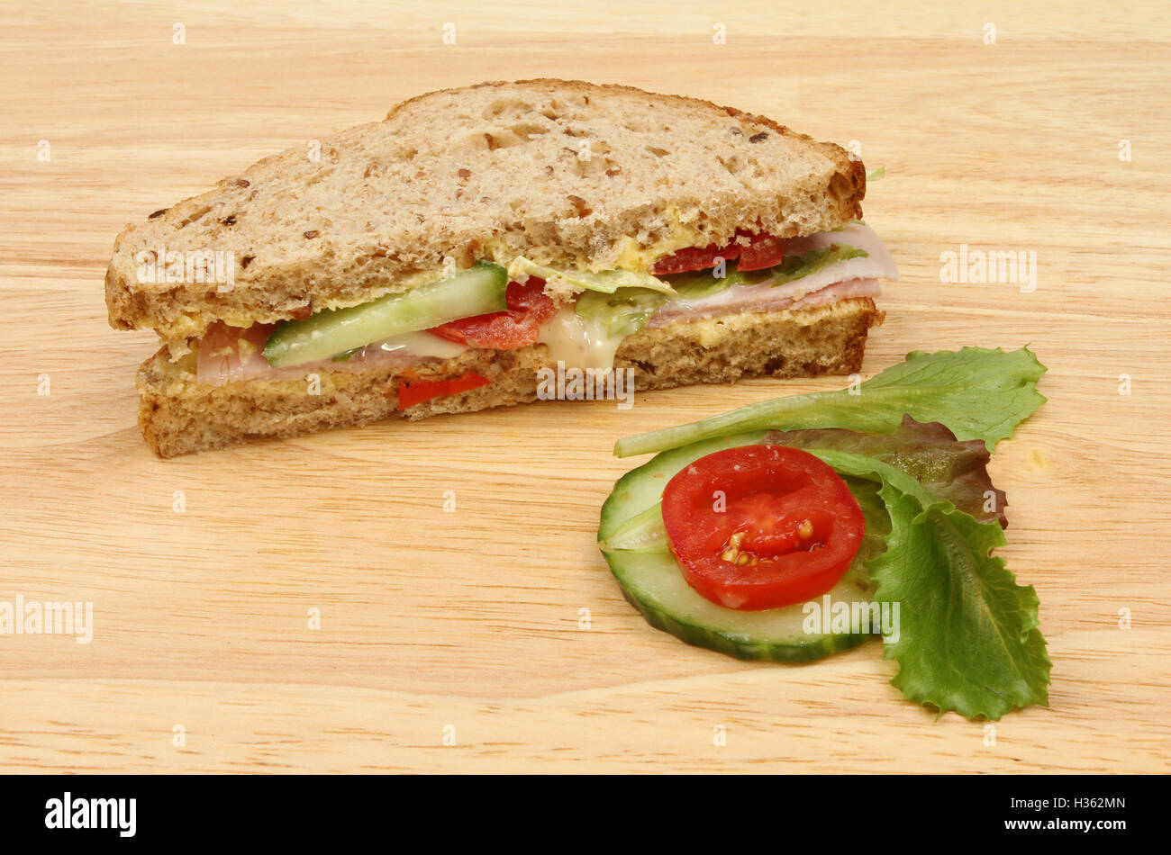 Schinken-Salat-Sandwich mit Gurke, Salat und Tomate garniert auf ein Schneidbrett aus Holz Stockfoto