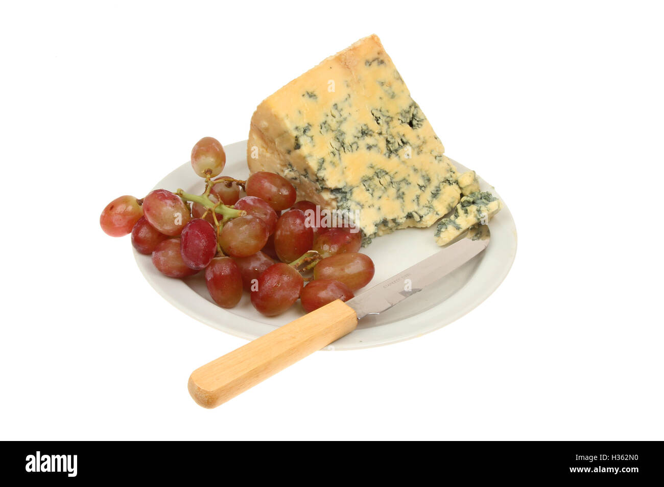 Stilton Käse und Trauben mit einem Käsemesser auf einem Teller isoliert gegen weiß Stockfoto