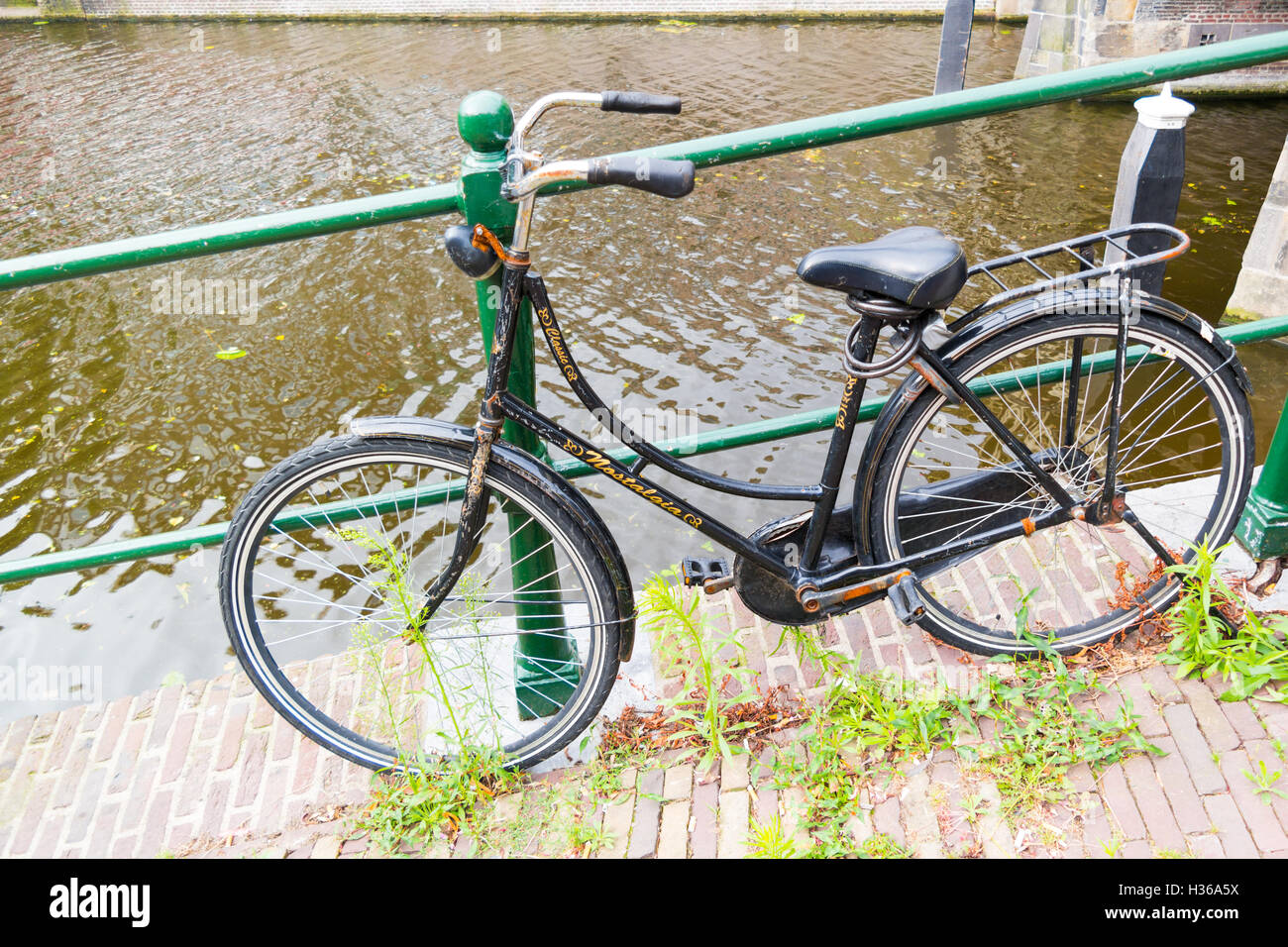 Altes Fahrrad durch Geländer geparkt am Kai des Kanal - weed und Zigarettenstummel auf der Straße in der Innenstadt von Leiden, Niederlande Stockfoto