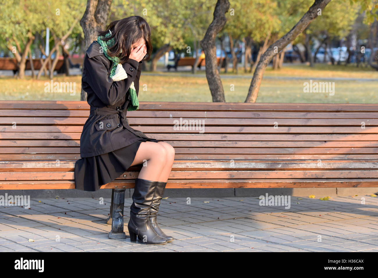 Mädchen auf Bank sitzt und bedeckt sein Gesicht mit den Händen Stockfoto