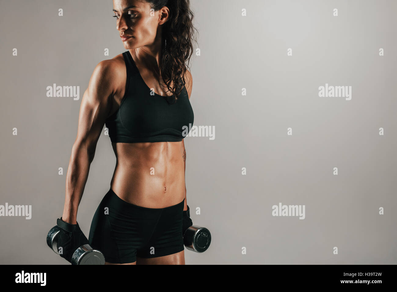 Drei Viertel Blick auf wunderschöne sportliche Frau ruht mit Chrome fertige Hantel Gewichte an ihre Seiten während aussehende ov Stockfoto