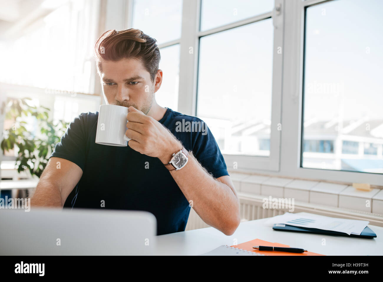 Junger Geschäftsmann, trinken Kaffee und arbeiten am Laptop im Büro. Männliche Führungskraft arbeitet an seinem Schreibtisch und Kaffee trinken. Stockfoto
