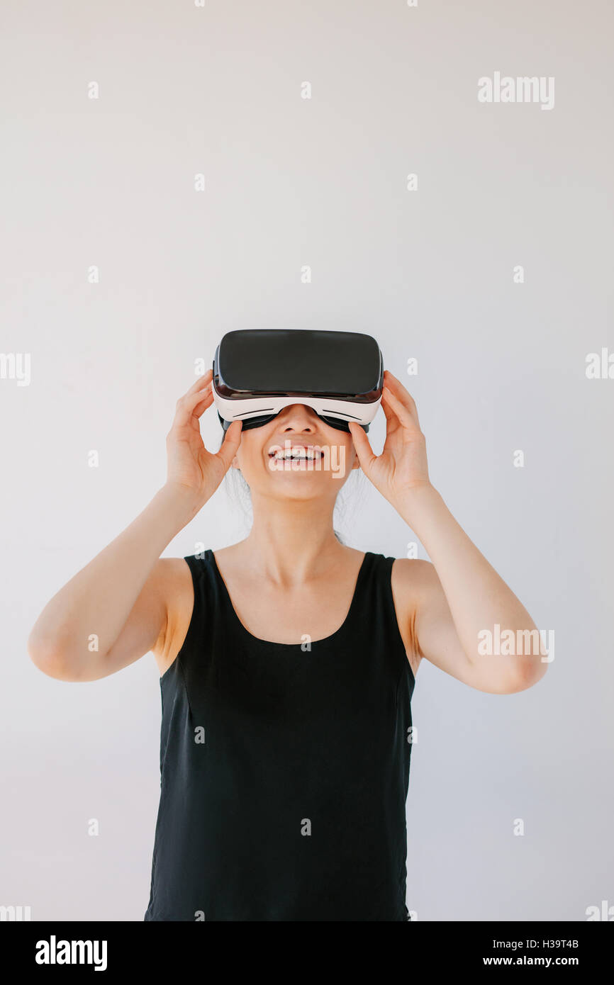 Vertikale Aufnahme der jungen Frau, die mit dem virtual-Reality-Gerät. Glückliche Frauen tragen VR Brille vor grauem Hintergrund. Stockfoto