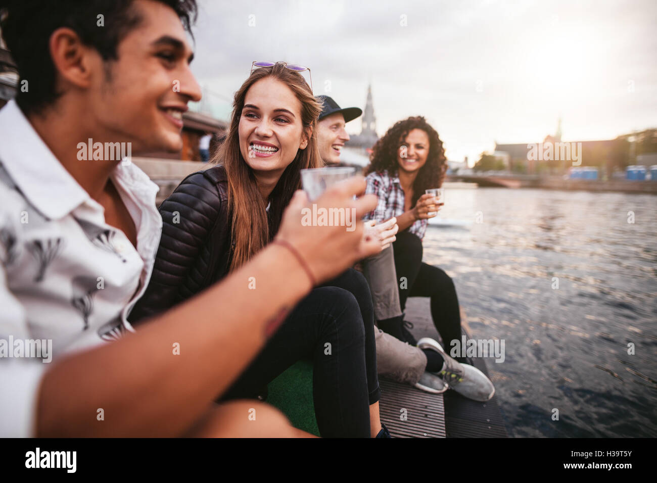 Schuss von junge Frau sitzt mit ihren Freunden, die Getränke. Gruppe von glücklich junge Menschen entspannen am See. Stockfoto