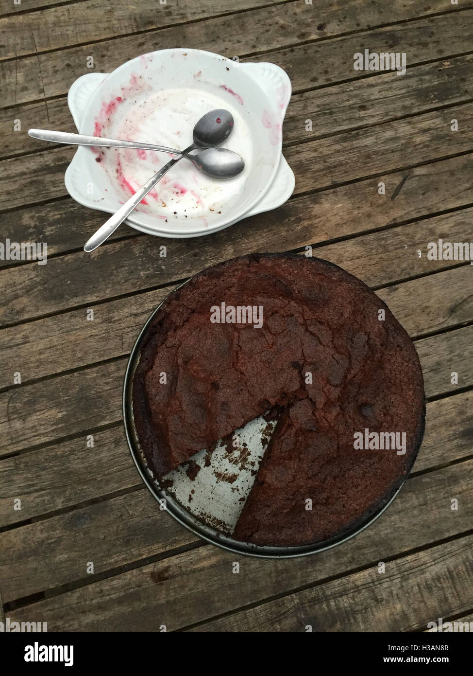 Schokoladenkuchen in Backform mit Teile fehlen und zwei leere Teller mit Löffel Stockfoto