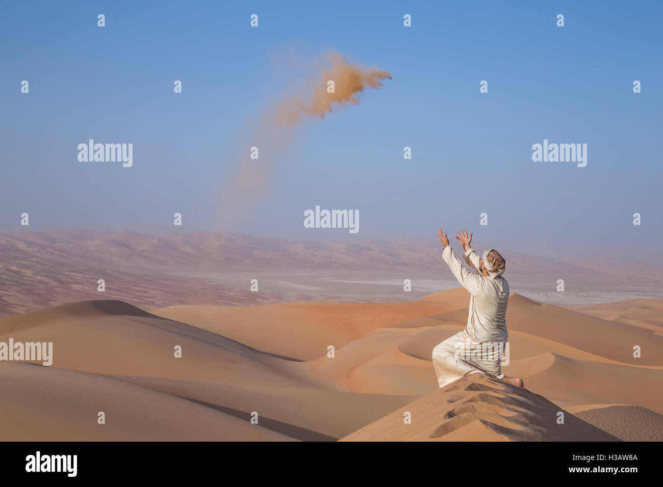Mann in traditioneller Kleidung in einer Wüste bei Sonnenaufgang, wirft sand Stockfoto