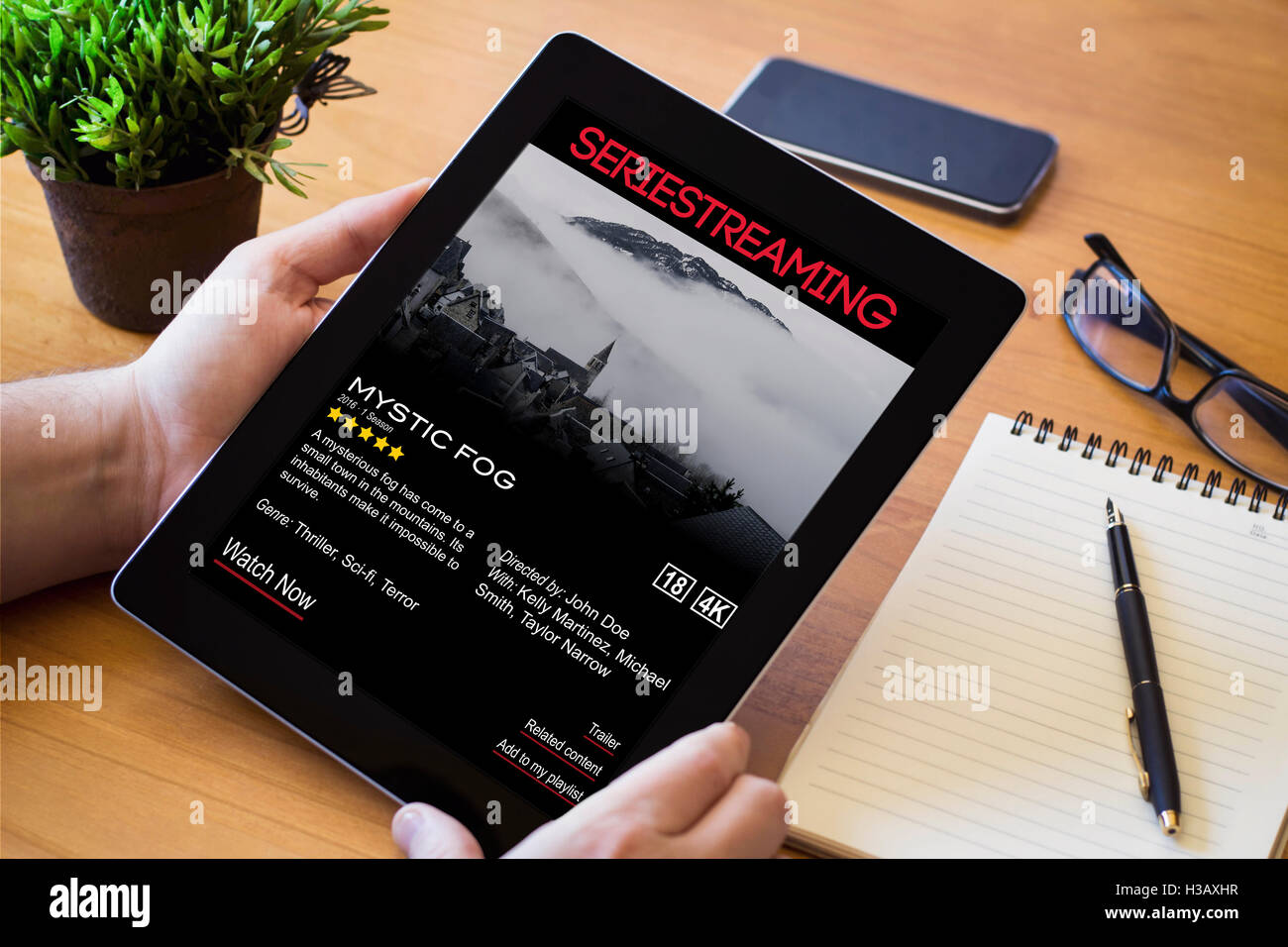 Hände eines Mannes hält ein Streaming-video-Gerät über eine hölzerne Workspace-Tabelle. Alle Bildschirm-Grafiken bestehen. Stockfoto