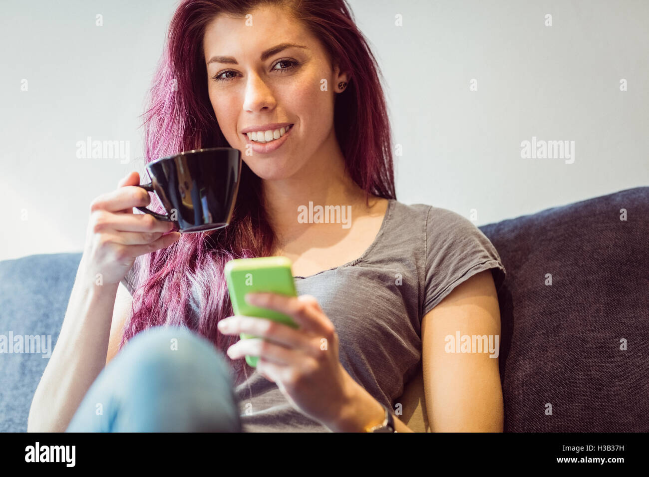 Lässige Frau trinken eine Tasse Kaffee mit einem smartphone Stockfoto