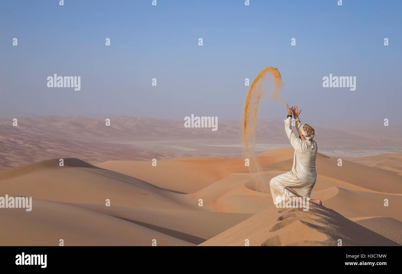 Mann in traditioneller Kleidung in einer Wüste bei Sonnenaufgang, wirft sand Stockfoto