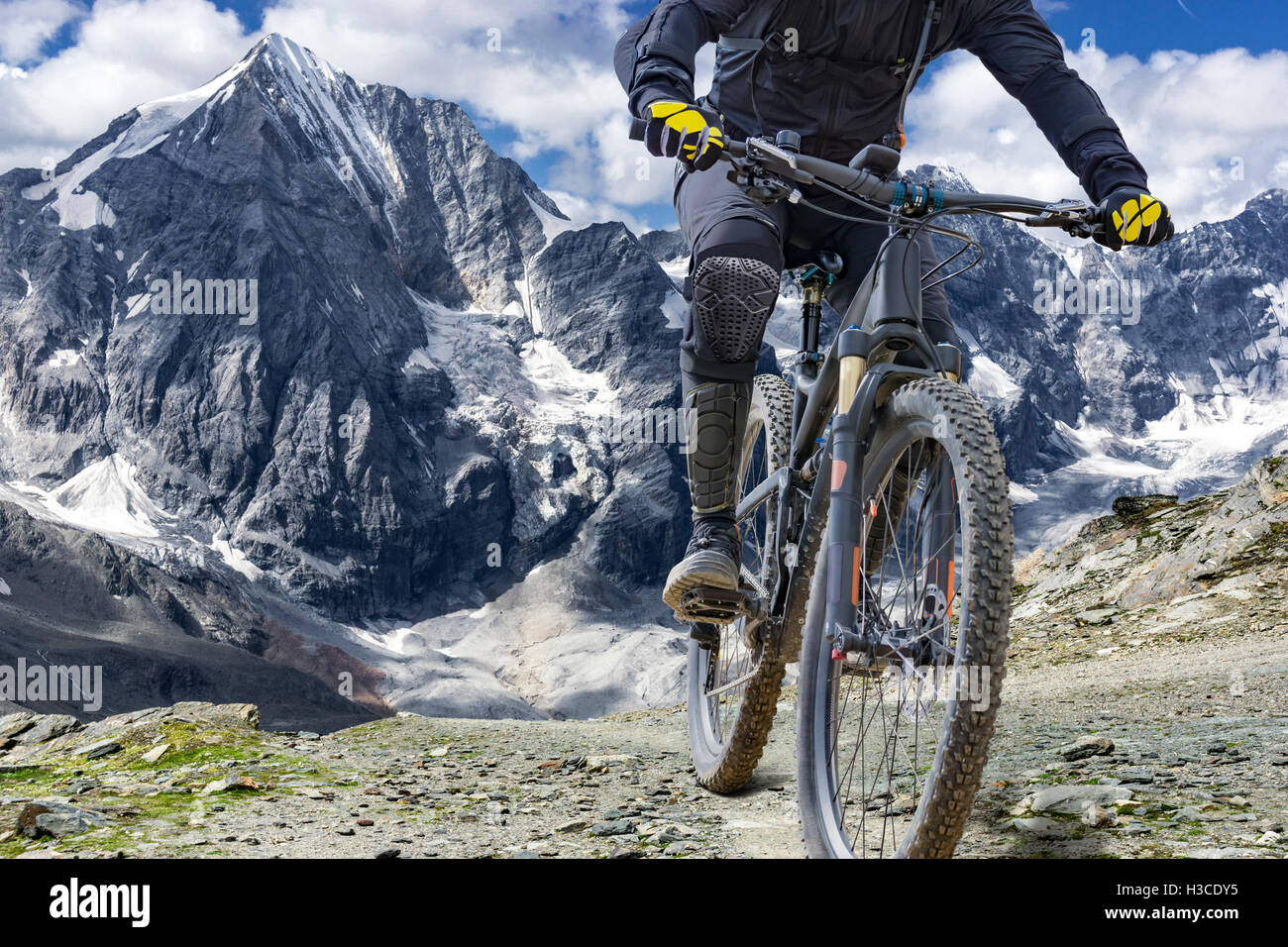 Mountain-Bike-Fahrer mit Protektoren fährt ein Singletrail in großer Höhe. Der Hintergrund ist das Bergmassiv "Ortler" Stockfoto