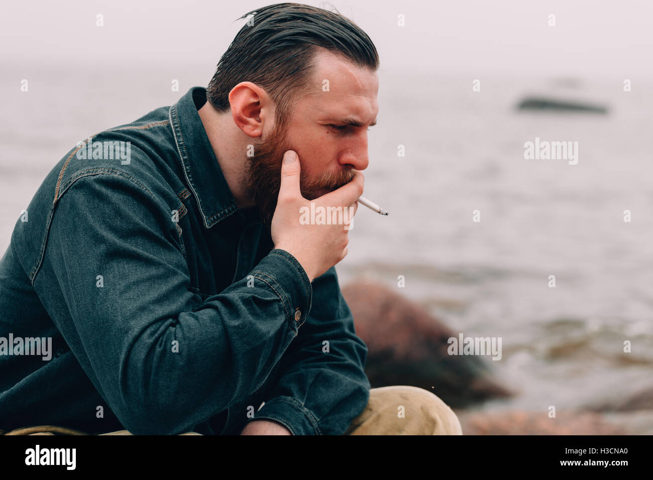 Ernster bärtigen Mann Rauchen einer Zigarette am Strand Stockfoto