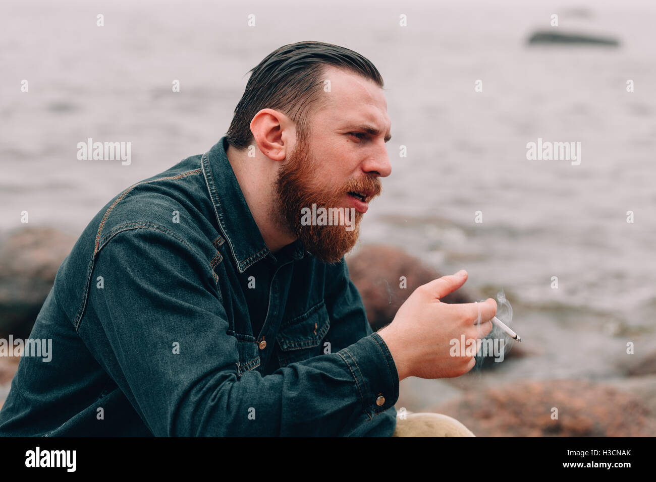 Ernster bärtigen Mann Rauchen einer Zigarette am Strand Stockfoto
