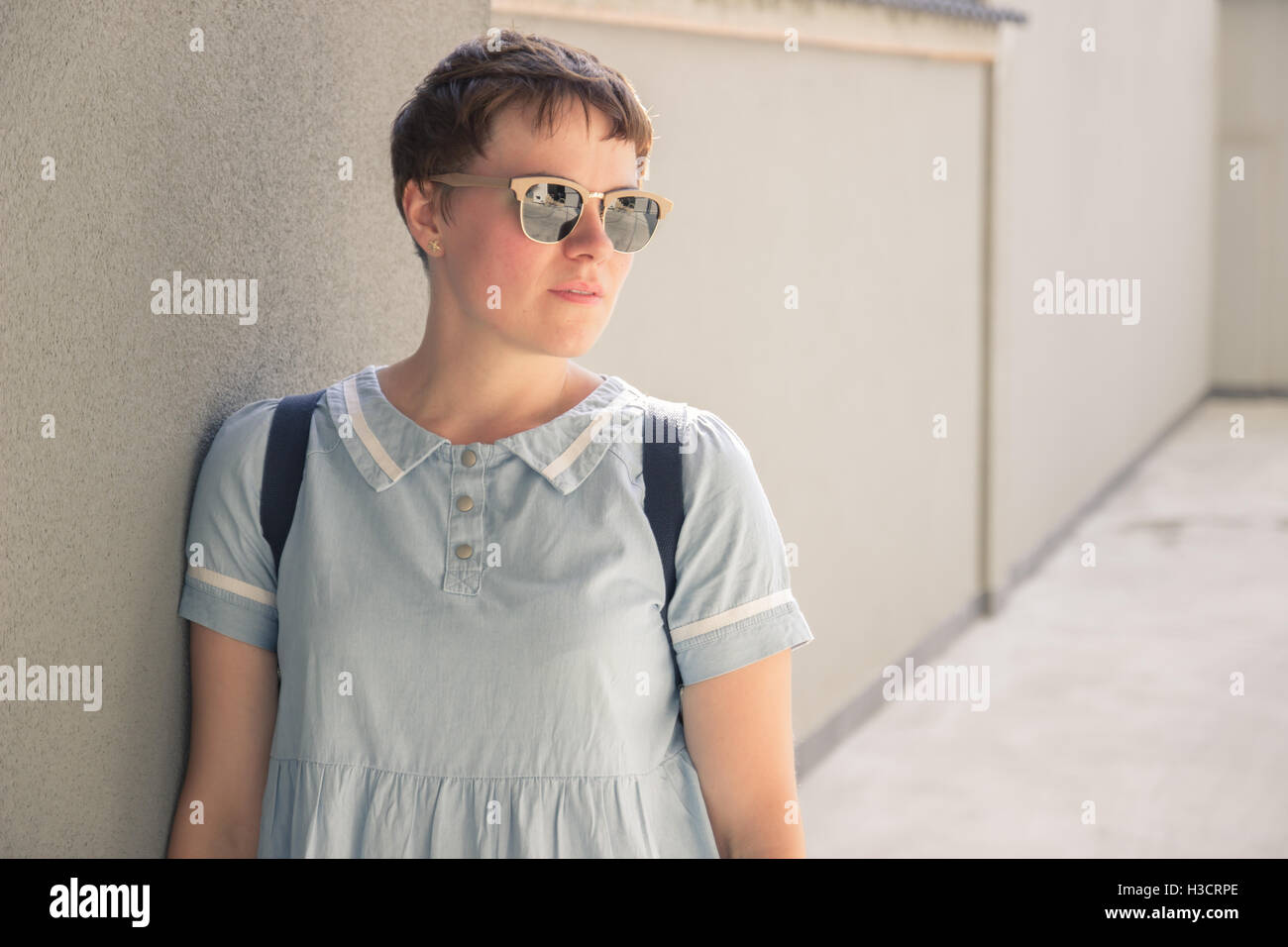 junge Frau-Mode-Blogger posiert stützte sich auf Wand Sonnenbrille einfach legere Kleidung Kleid Rucksack Stockfoto