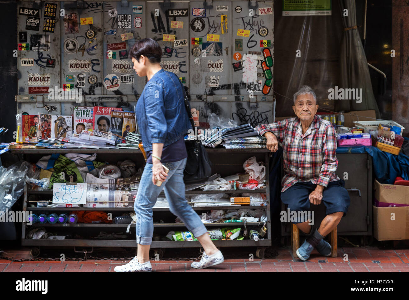 Frau vorbei ein Greis, der Zeitungen und Zeitschriften in Sheung Wan auf Hong Kong Island in Hongkong, China verkauft. Stockfoto