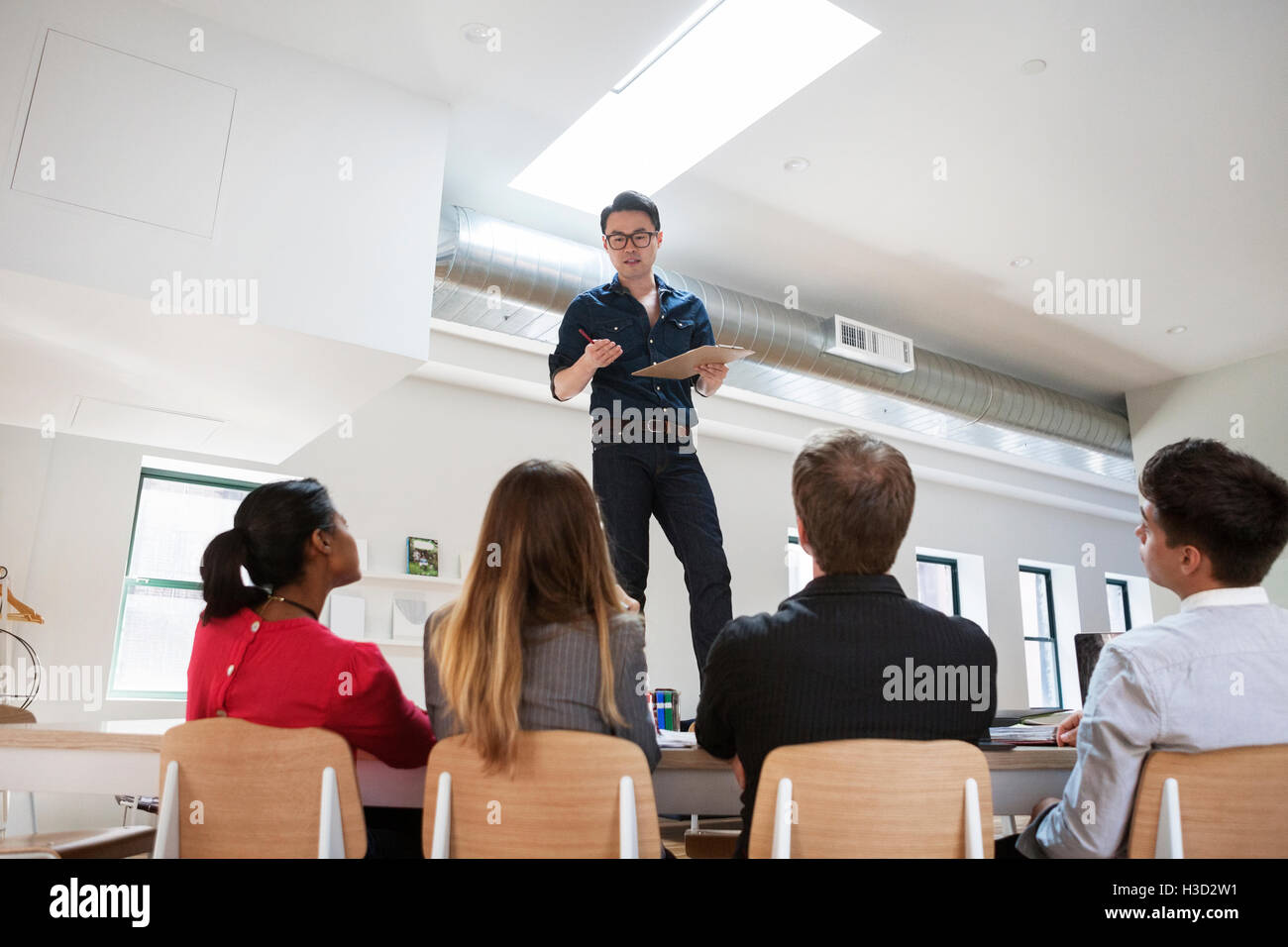 Geschäftsmann diskutiert mit Kollegen, während er im kreativen Büro auf dem Schreibtisch steht Stockfoto
