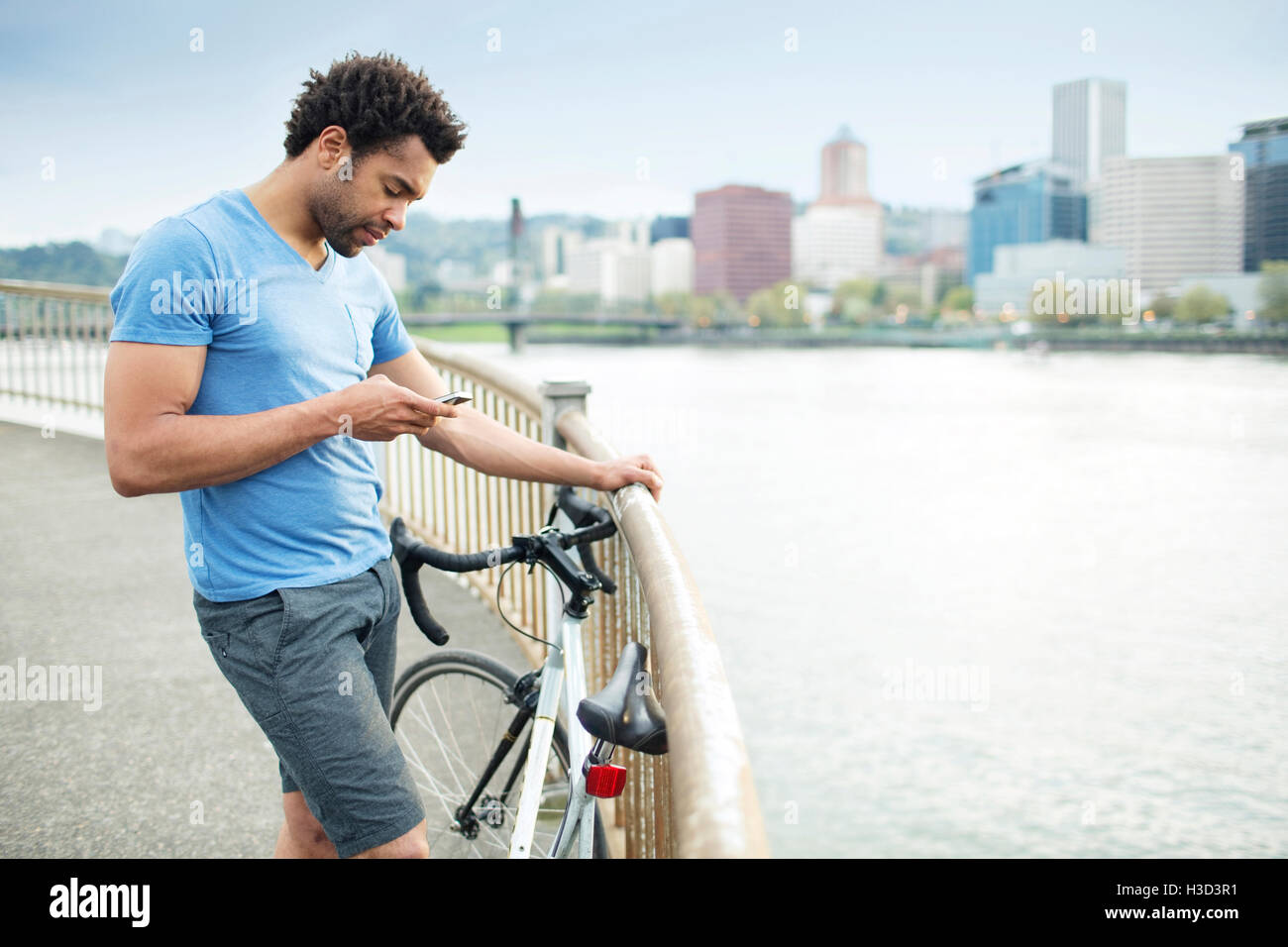 Athlet mit Smartphone stehend mit Fahrrad auf Brücke Fluss Stockfoto