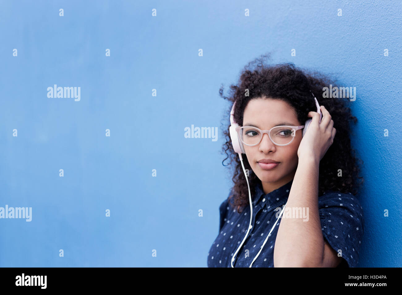 Nachdenkliche junge Frau Musik hören vor blauem Hintergrund Stockfoto