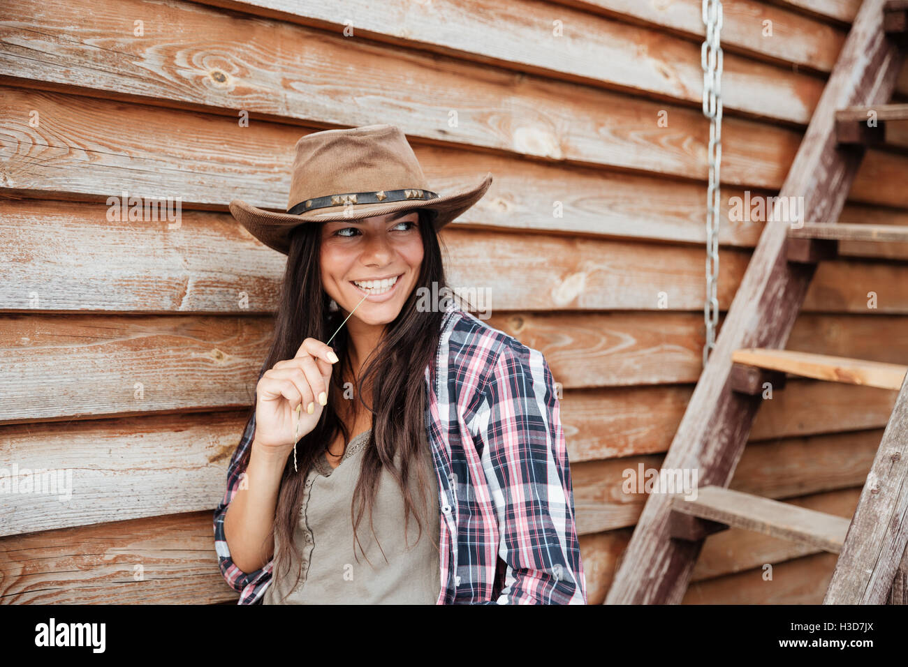 Hübsche junge Frau Cowgirl in Hut Stand in der Nähe des Hauses lächelnd Stockfoto