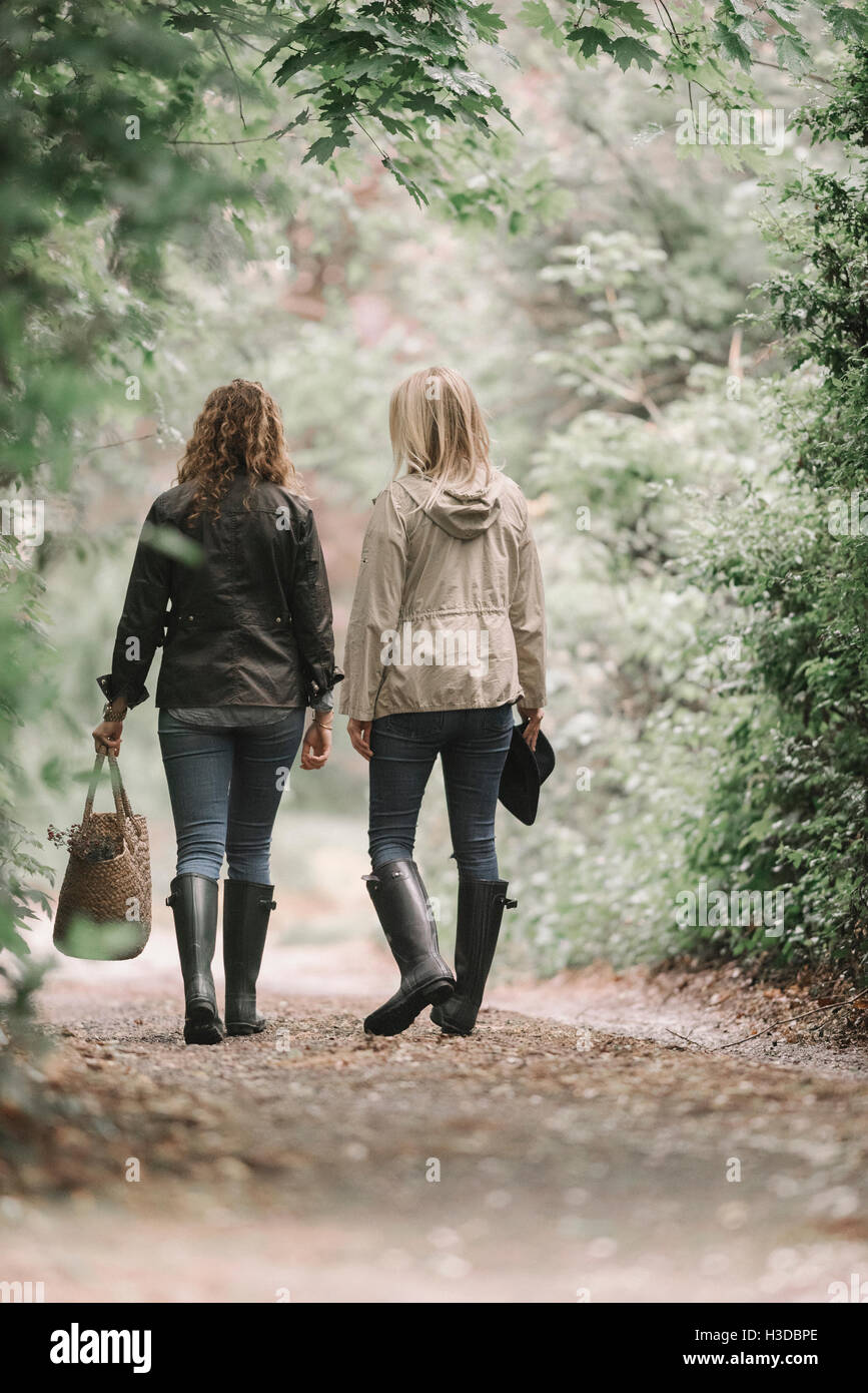 Zwei Frauen gehen in Mänteln und Stiefeln entlang einem Feldweg mit einem Korb. Stockfoto