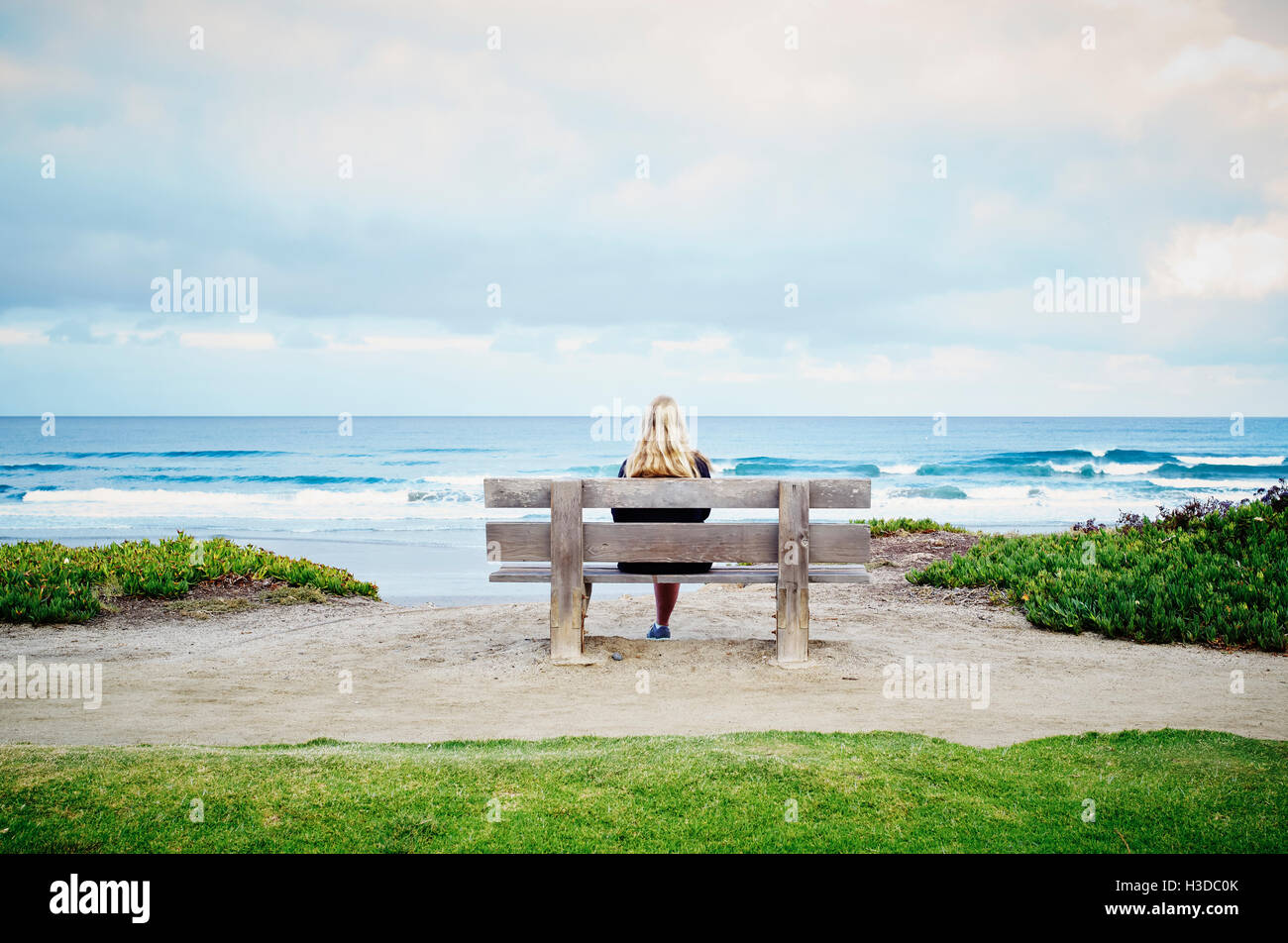 Rückansicht einer blonden Frau an einem Strand am Meer sitzen. Stockfoto