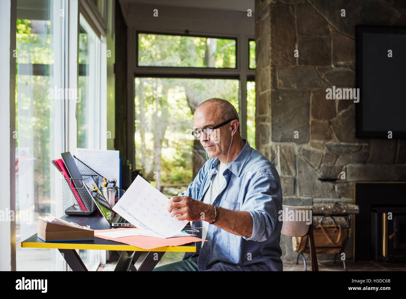 Ein Mann sitzt an einem Schreibtisch zu Hause arbeiten durch Papierkram sortieren. Stockfoto