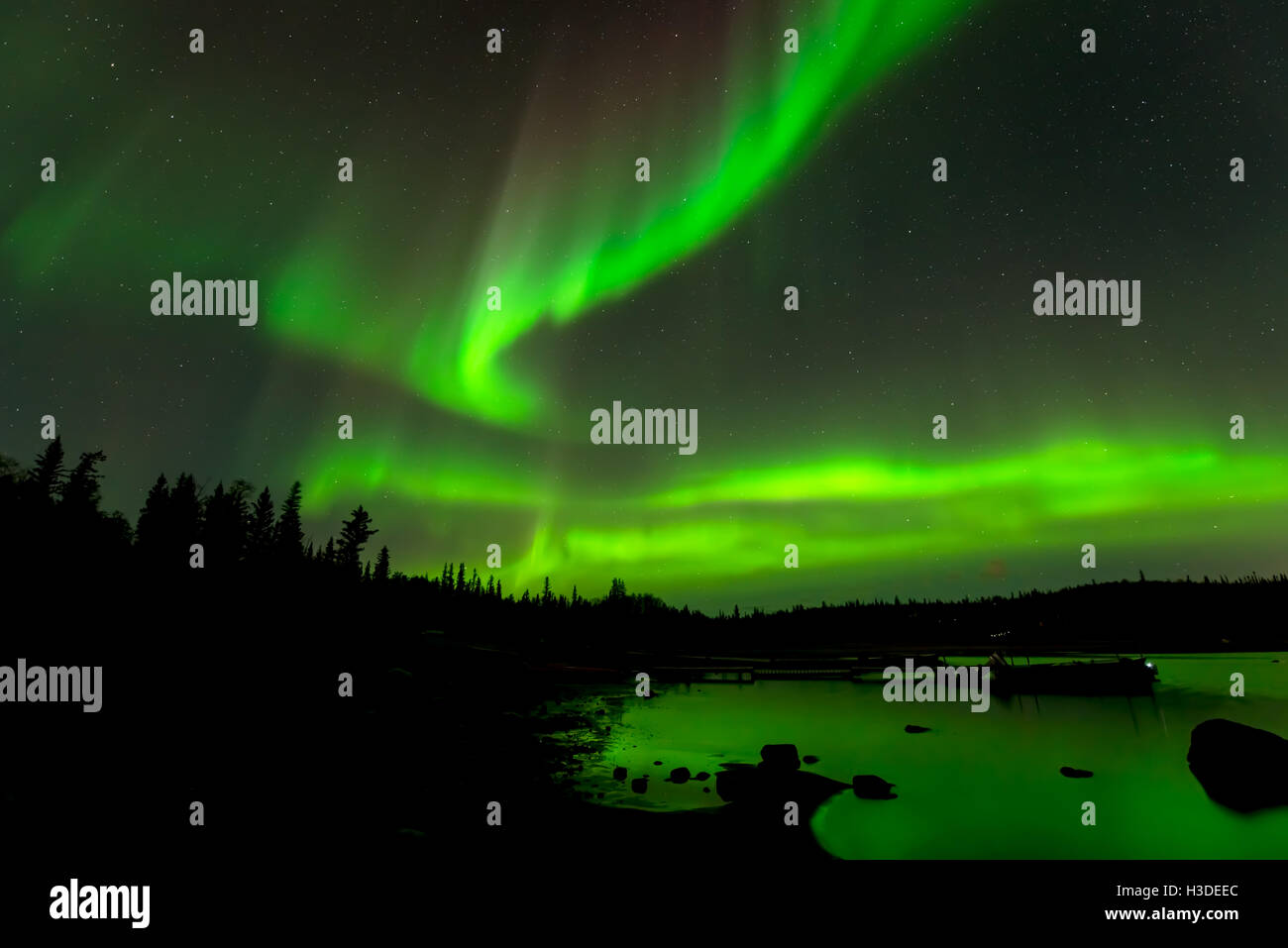 Tanzende Lichter - bunte Nordlicht Drop-down-Sternenhimmel über immergrünen Wald rund um einen See. Stockfoto