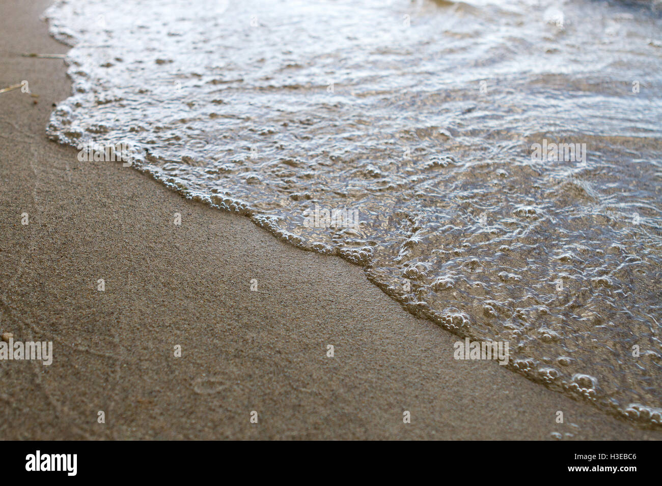 Strand mit ruhigen Wellen, glatten nassen Sand und Lichtreflexion auf dem Wasser Stockfoto