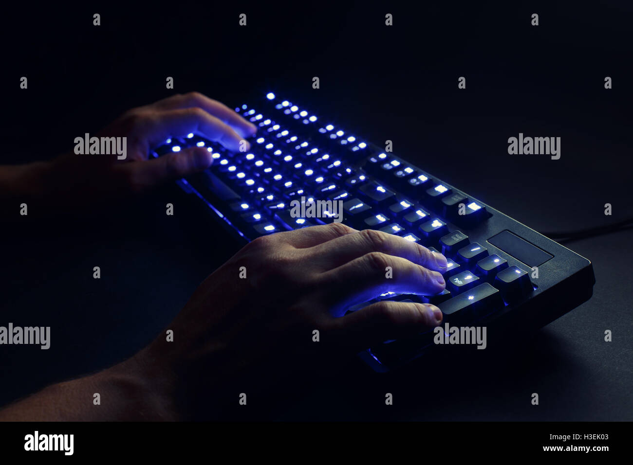 beleuchtete Tastatur. männlichen Händen tippen auf einen Computer. Hacker oder Programmierer bei der Arbeit. auf einem schwarzen Hintergrund. Stockfoto
