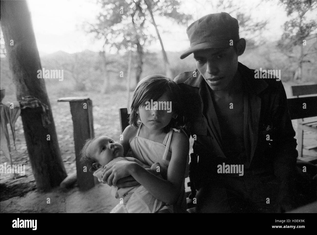 CHALATENANGO, EL SALVADOR, FEB 1984: - innerhalb der FPL Zonen der Steuerung A FPL Guerillakämpfer machen einen Besuch zu Hause sitzt mit seinem Bruder Schwester und Baby.   Foto: Mike Goldwater Stockfoto