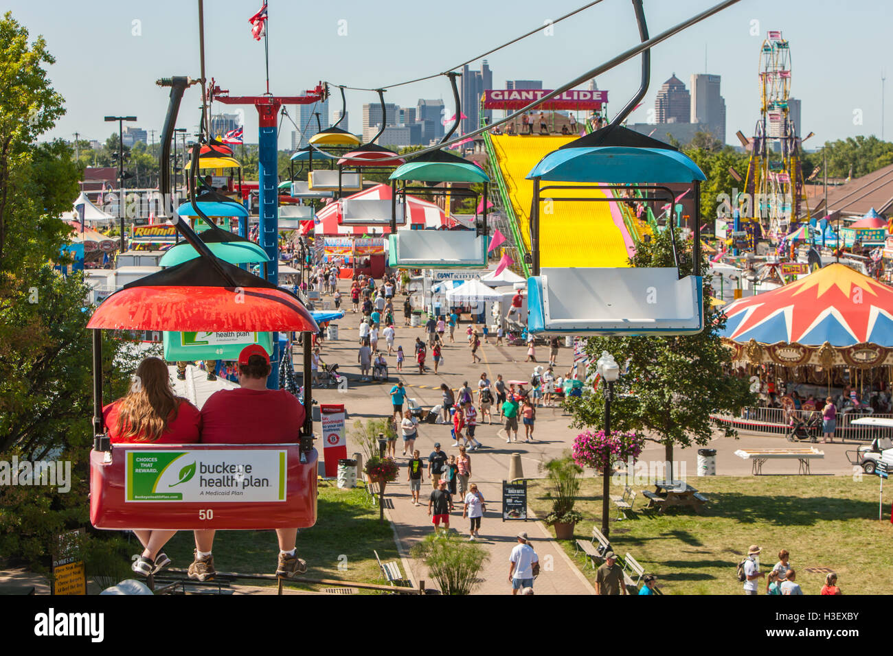 Die Menschen genießen Attraktionen und Fahrgeschäfte auf der Midway von der Ohio State Fair, mit der Skyline im Hintergrund in Columbus, Ohio. Stockfoto