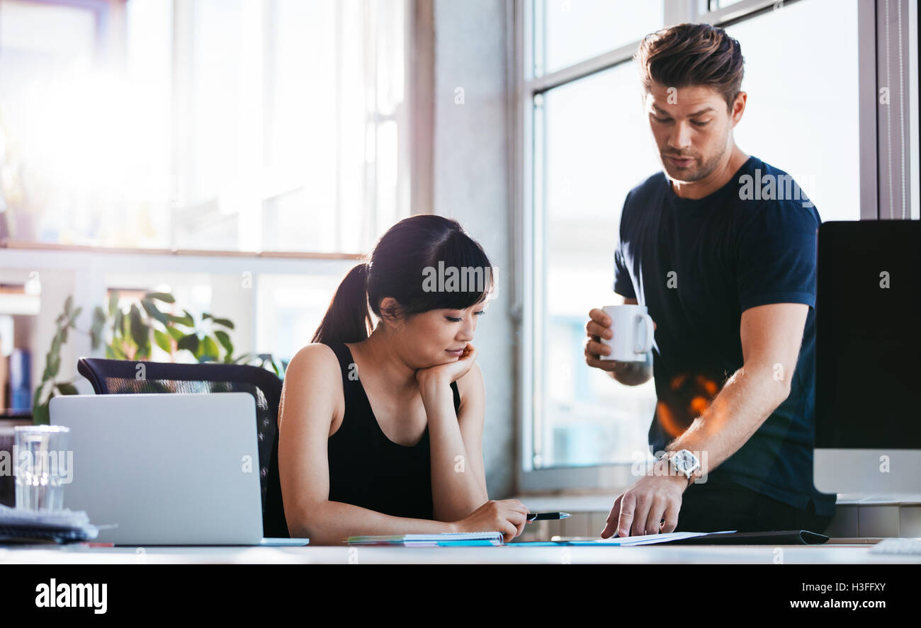 Schuss von asiatischen Geschäftsfrau sitzt an ihrem Schreibtisch mit männlichen Kollegen hilft ihr mit neuen Geschäftsideen. Zwei junge executive wor Stockfoto