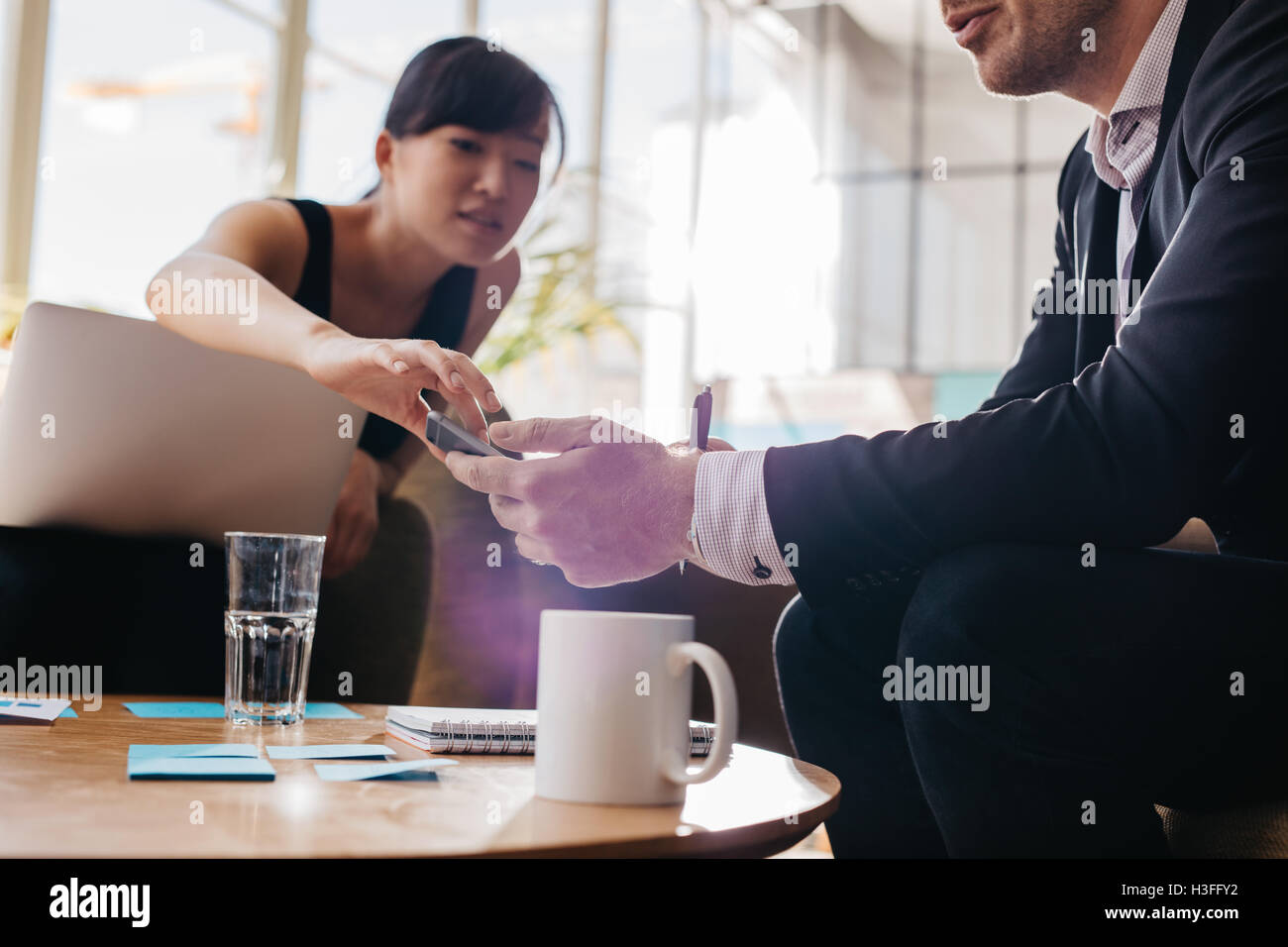 Schuss von jungen Geschäftsleuten mit Handy beim sitzen zusammen im Büro Lobby beschnitten. Konzentrieren Sie sich auf Hände und Handy. Stockfoto