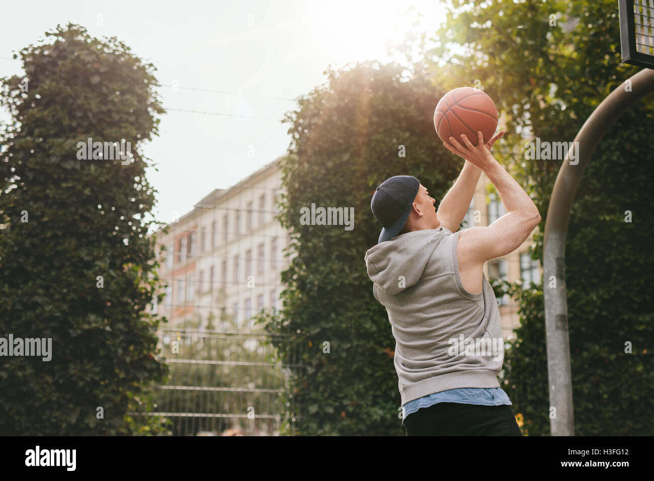 Bild eines Streetball-Spieler spielen auf Freiplatz. Junger sportlicher Mann unter Sprungwurf auf Basketballplatz. Stockfoto