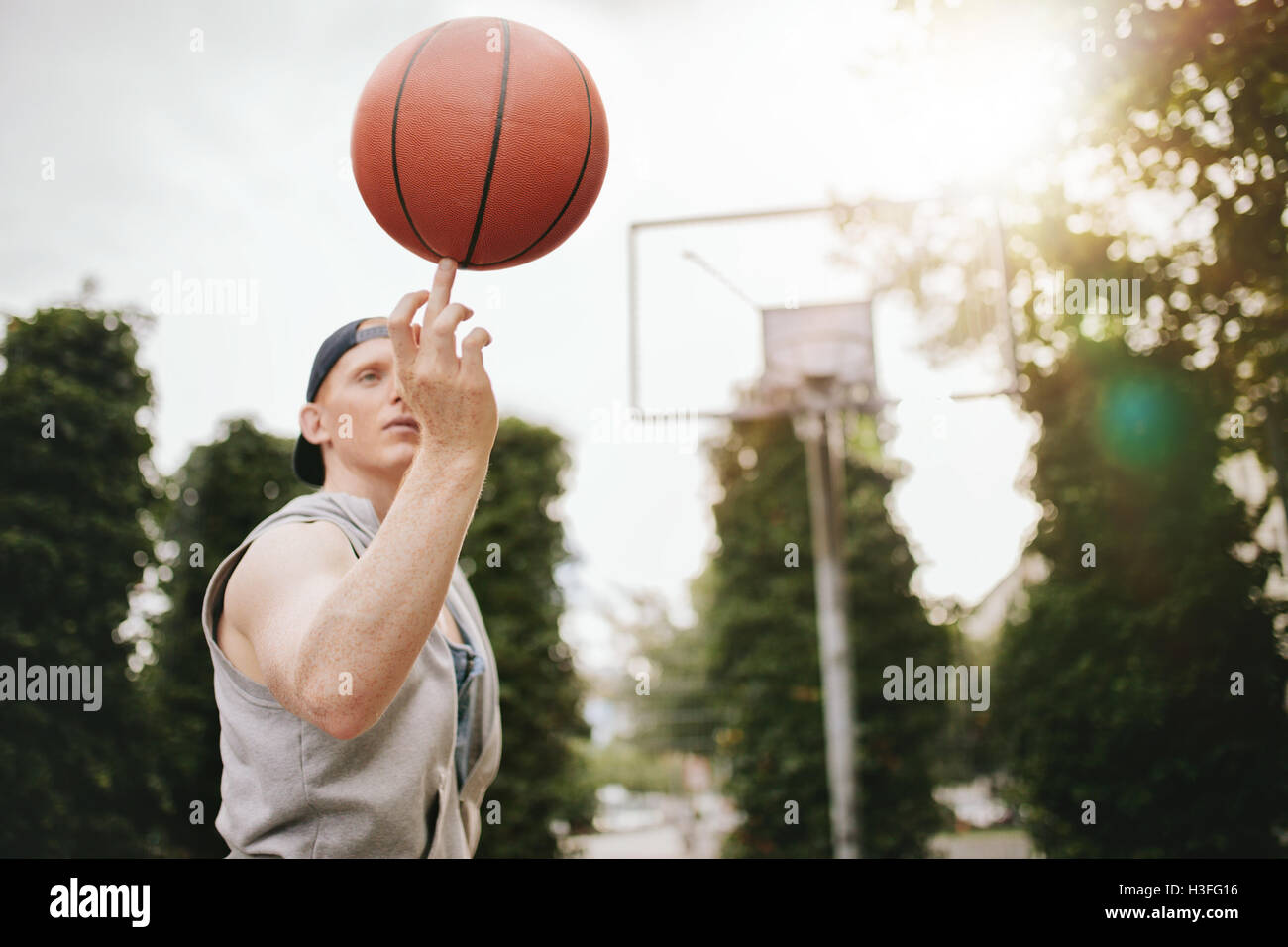 Junger Mann Ausgleich Basketball an seinem Finger auf Freiplatz. Streetball Spieler den Ball drehen. Basketball im Vordergrund. Stockfoto