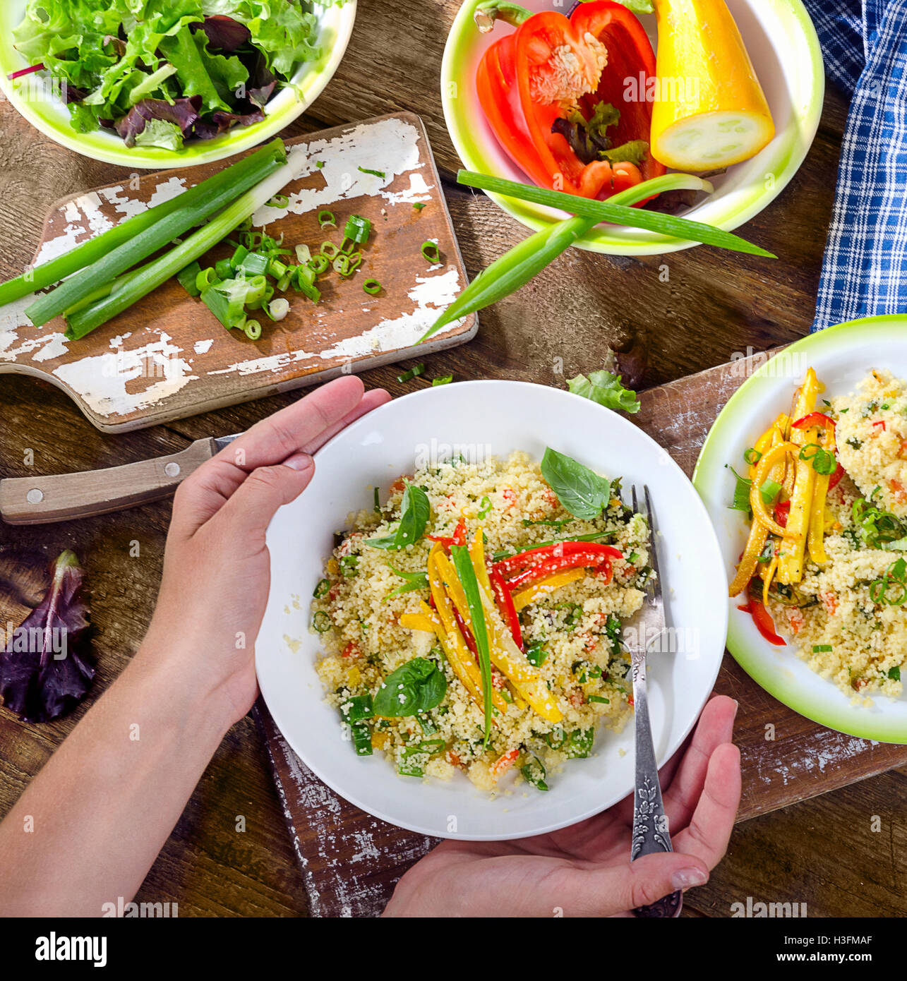 Hände halten Couscous mit Gemüse auf einem Holztisch. Ansicht von oben Stockfoto