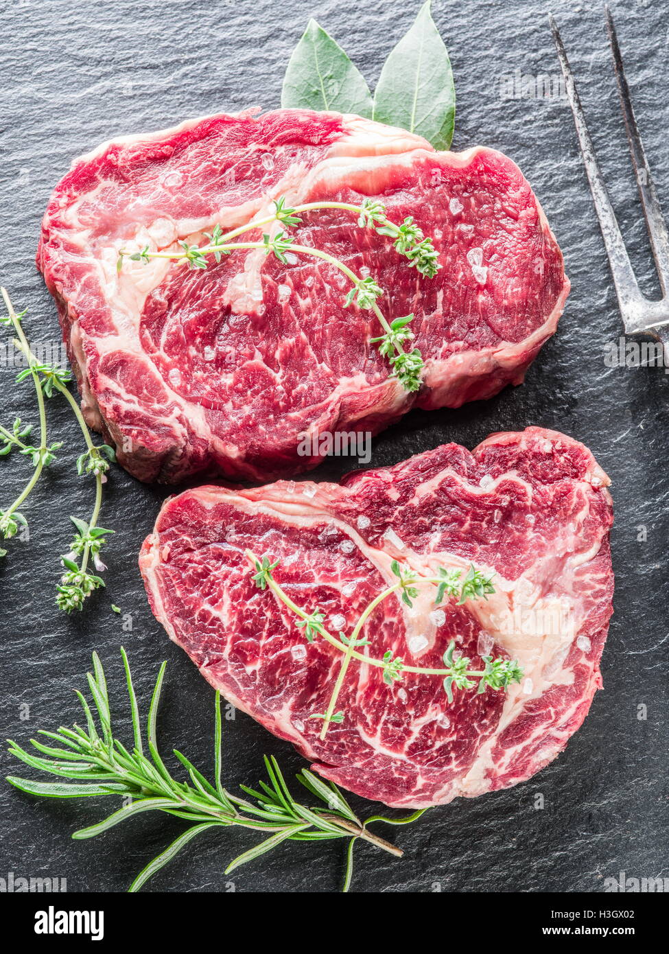 Rib-Eye-Steaks mit Gewürzen auf dem schwarzen Hintergrund. Stockfoto