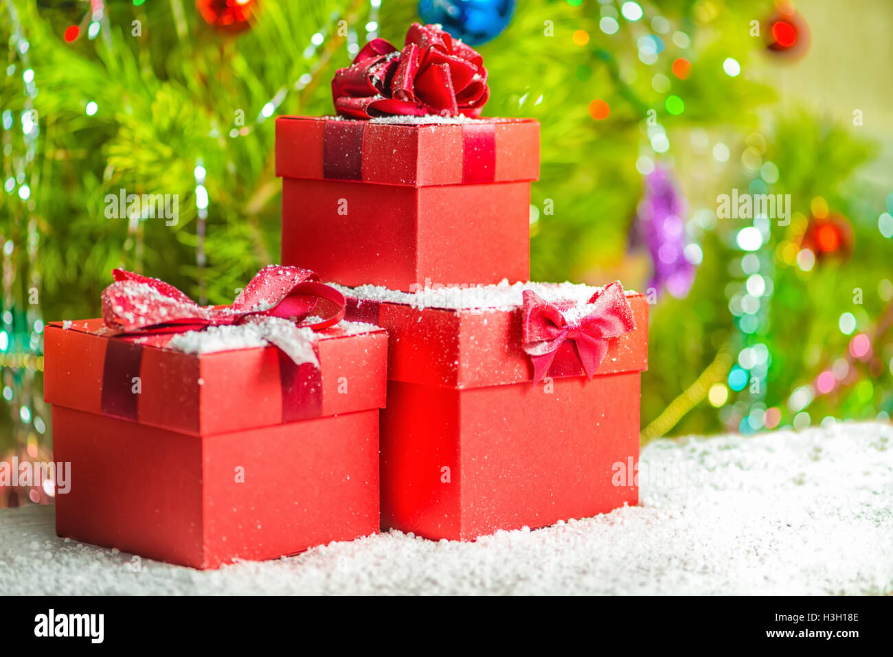 Konzept neue Jahr Urlaub von roten Geschenk-Boxen mit Bogen auf hölzernen Hintergrund und Schnee über geschmückter Weihnachtsbaum, Nahaufnahme Stockfoto