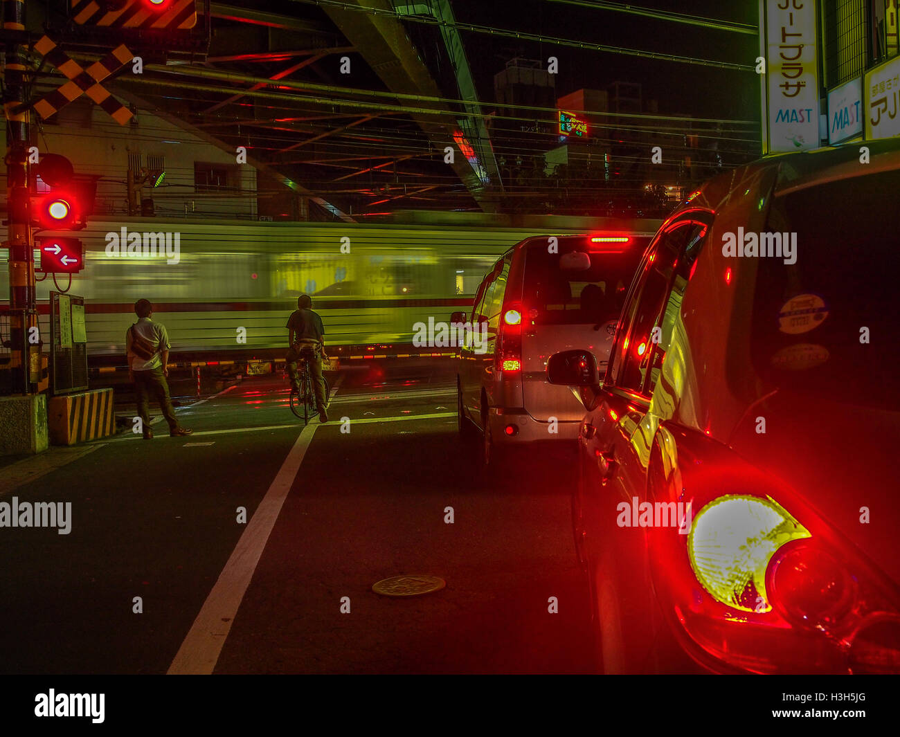 rote Ampeln flare als Autos und Radfahrer und einem Fußgänger warten auf eine Geschwindigkeit erlauben Nachtzug zu überqueren, Bahnpass Kawagoe Saitama japan Stockfoto