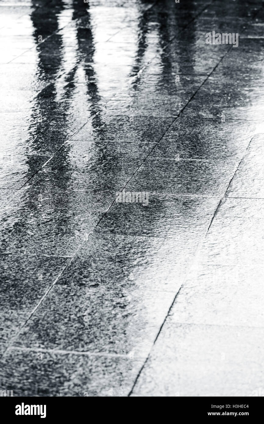 nassen Straßenpflaster mit Regentropfen Plätschern in Pfützen bei schlechtem Wetter Stockfoto