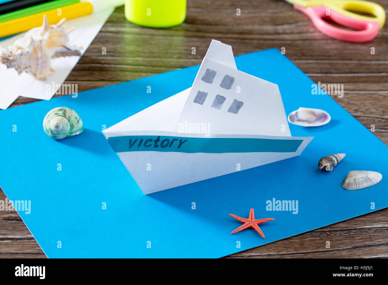 Papierschiff basteln, Origami. Kleber, Schere, Papier, Seesterne und  Muscheln auf einem Holztisch. Kinder Kunst-Projekt, ein Handwerk für  Stockfotografie - Alamy