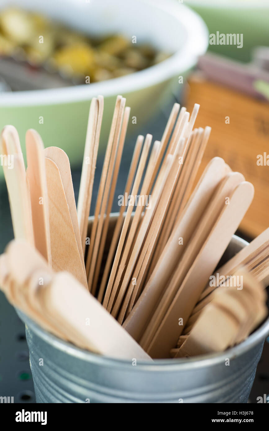 hölzerne Lollipop sticks in einem Metall Glas mit einem Griff mit Schüsseln mit Essen und verschiedene Gegenstände im Hintergrund Stockfoto