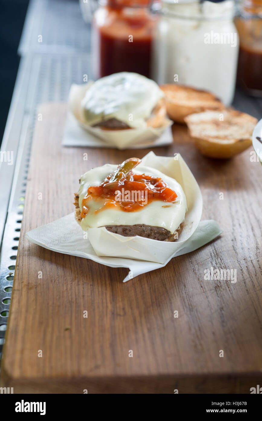 Cheeseburger mit Tomaten-Salsa in einer weißen Essbrett auf einer Serviette auf einer Holzfläche mit anderen Burgern und Saucen in der Hinterg Stockfoto