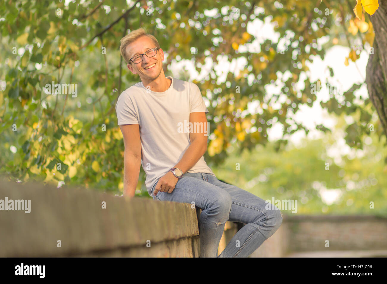 Sonnigen Tag ein junger Mann im freien Sommer sitzen Freizeitkleidung weißen T-shirt jeans Stockfoto