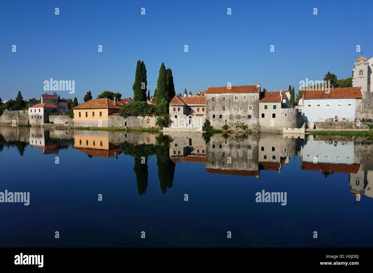 Mediterrane steinerne Stadtmauer spiegelt sich in einer schönen sauberen Fluss mit blauem Himmel Bäumen und alten Steinhäusern. Stockfoto