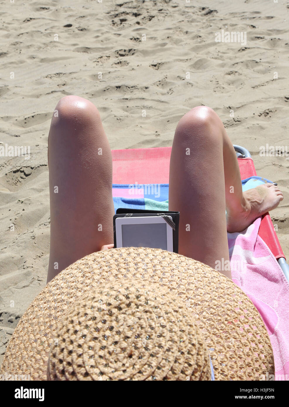 junge Frau mit Strohhut und langen Beinen während des Lesens ein ebook Stockfoto