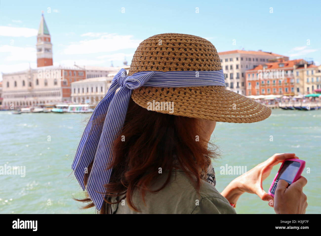 junge Frau mit langen braunen Haaren und einem breiten Strohhut verwendet das Smartphone ein Bild schicken, die Sie nur in Venedig Ita getroffen haben Stockfoto