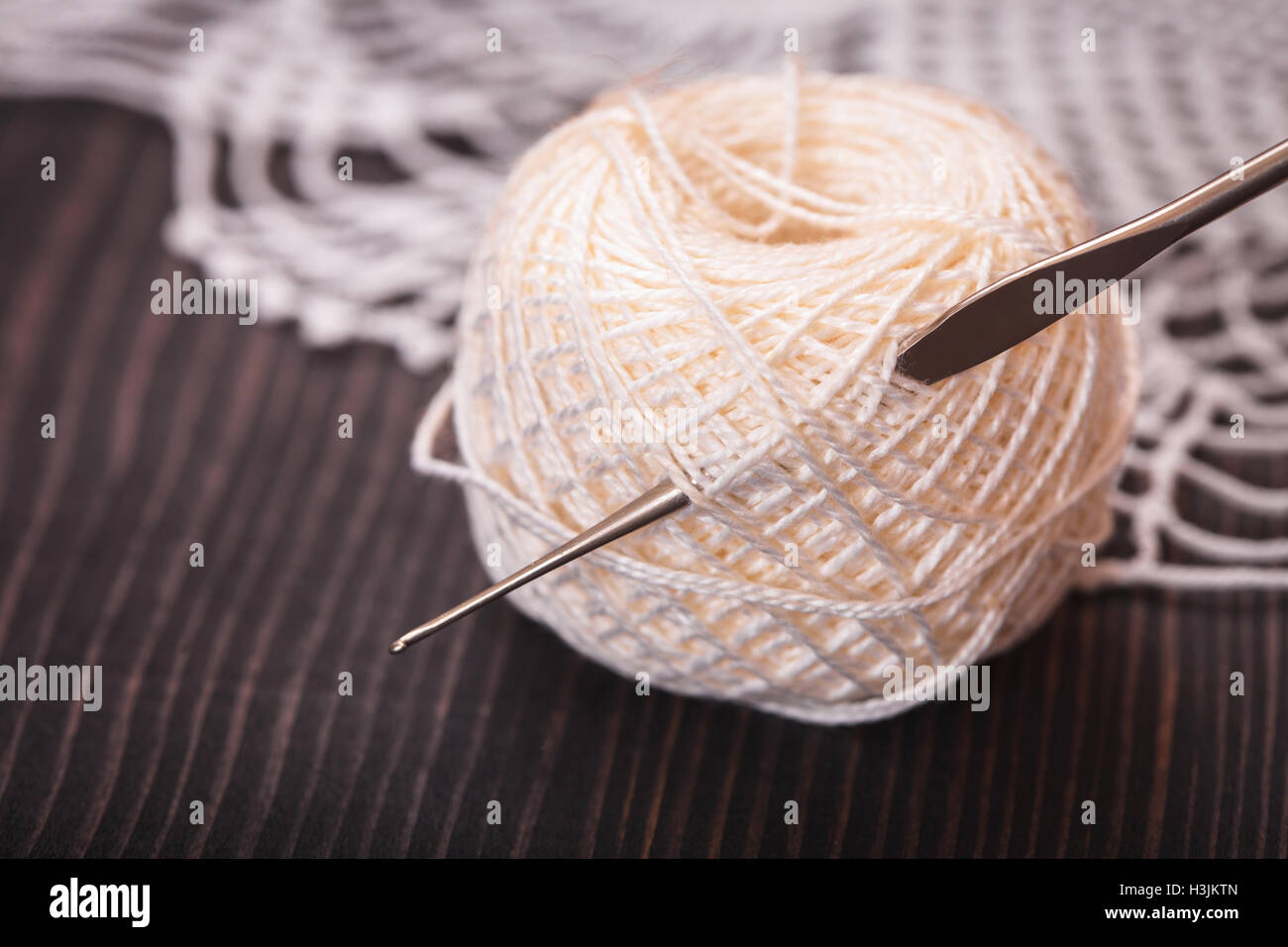 Strang aus weißen Garn und Häkelnadel auf einem Holztisch Nahaufnahme Stockfoto