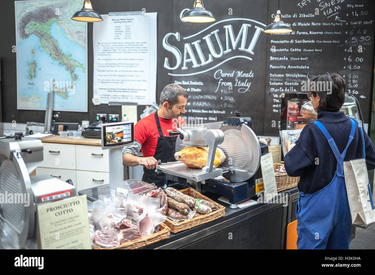 Borough Market, London UK Verkäufer schneiden das Stück Schinken auf der geschnittenen Maschine für seine Frau-Kunden Stockfoto