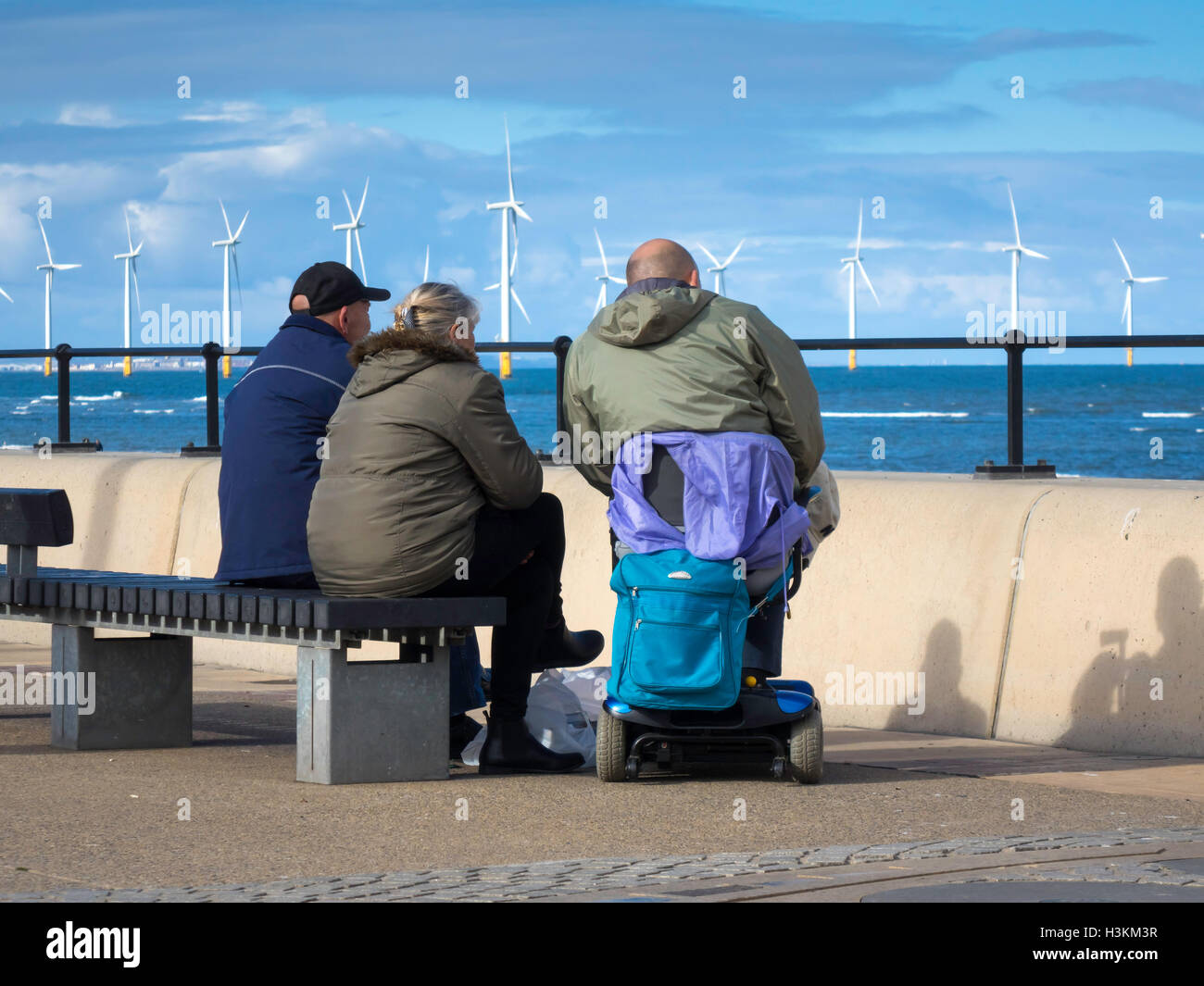 Zwei Männer und eine Frau sitzen auf der Redcar-Promenade, Blick auf das Meer an einem kühlen Herbsttag. Stockfoto